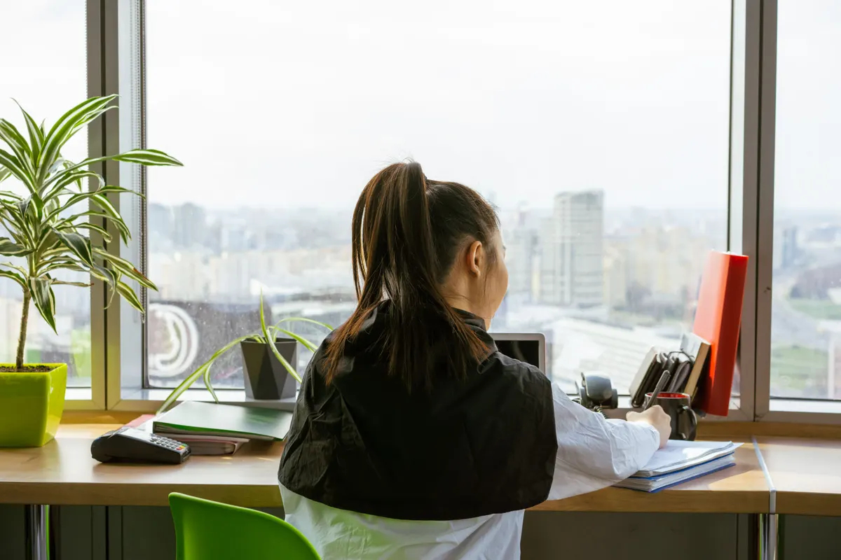 Someone writing at a desk beside a large window overlooking a city
