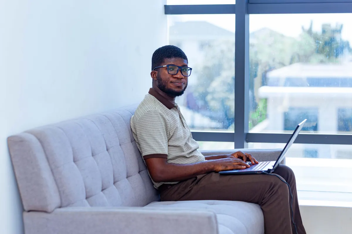 A person working on a laptop beside a window in a bright apartment