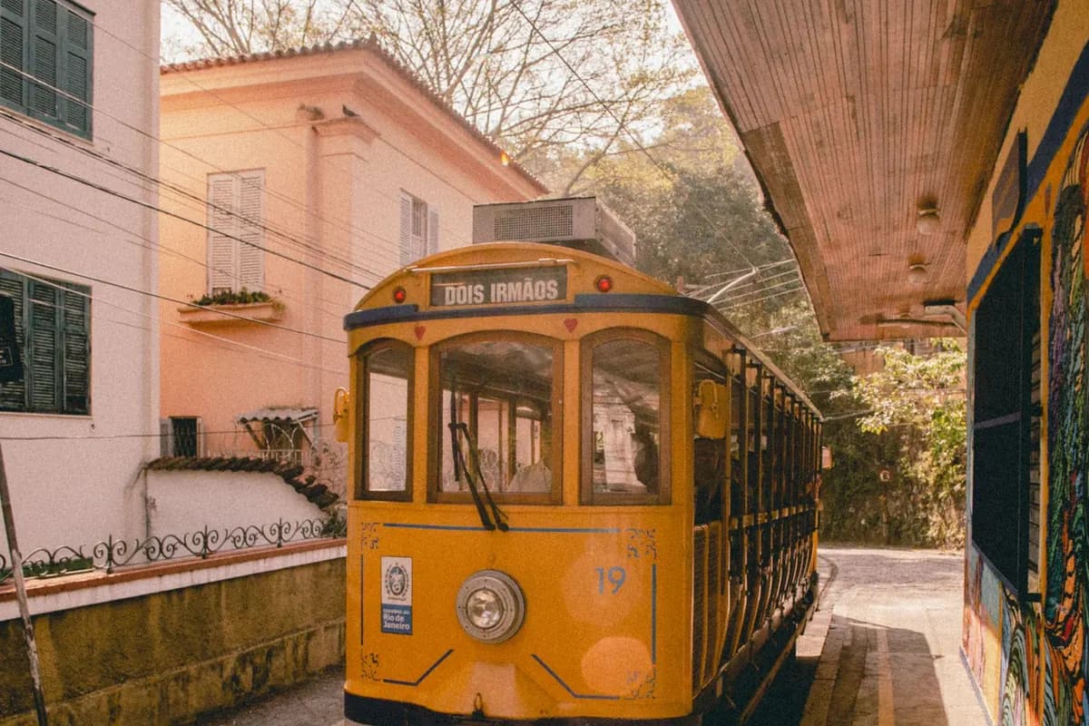 A yellow Santa Teresa tram on its tracks beside pastel colonial houses in Rio de Janeiro