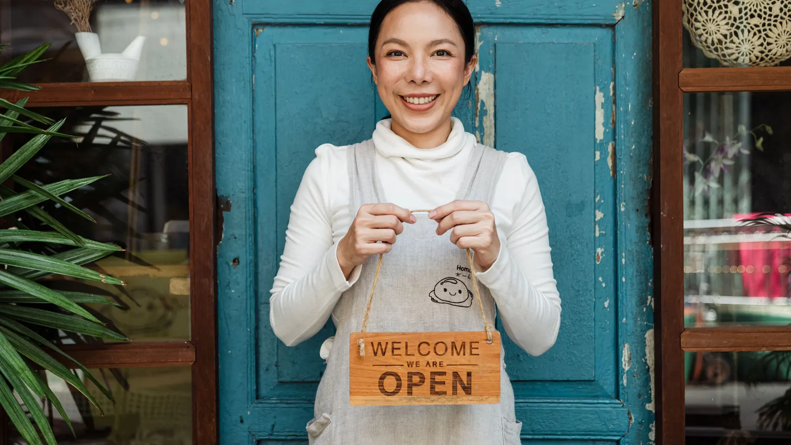 A small business owner standing at the entrance of her café holding an open sign